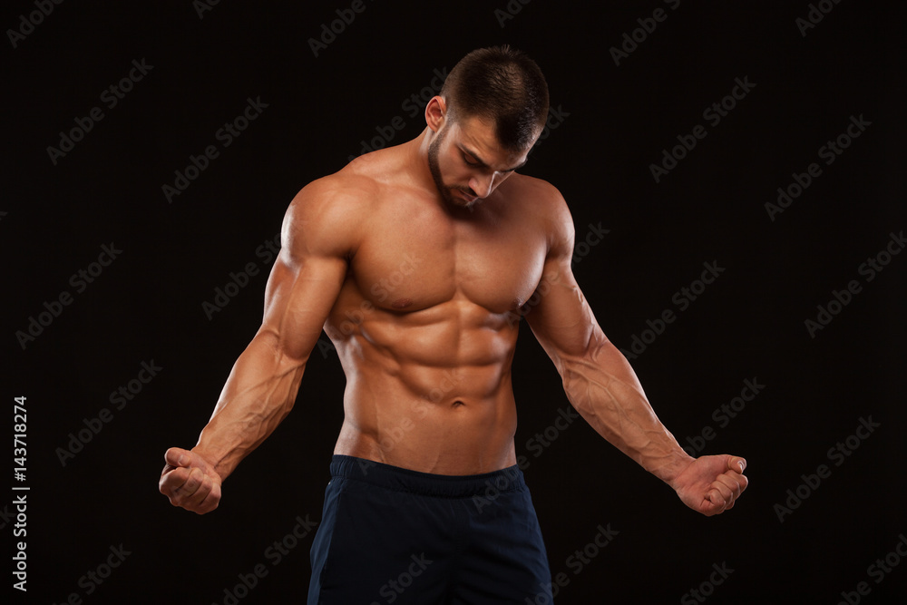 Fototapeta premium Strong Athletic Man Fitness Model Torso showing six pack abs. isolated on black background with copyspace is looking at himself