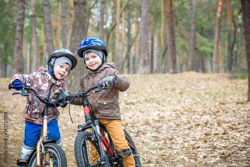 Two little siblings having fun on bikes in autumn or spring forest. Selective focus on boy.