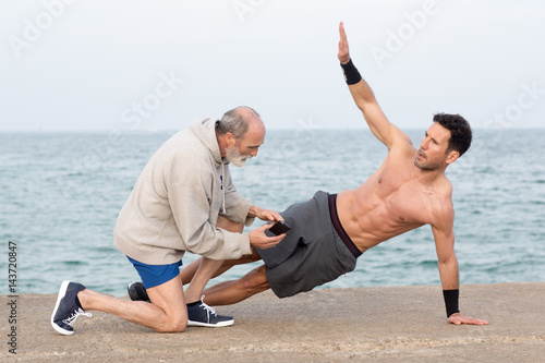 Mann macht seitliche Planke draußen am Meer mit Coach