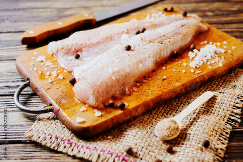 Fresh raw fish, fillet of hake with spices, black pepper and salt on a wooden board, background 