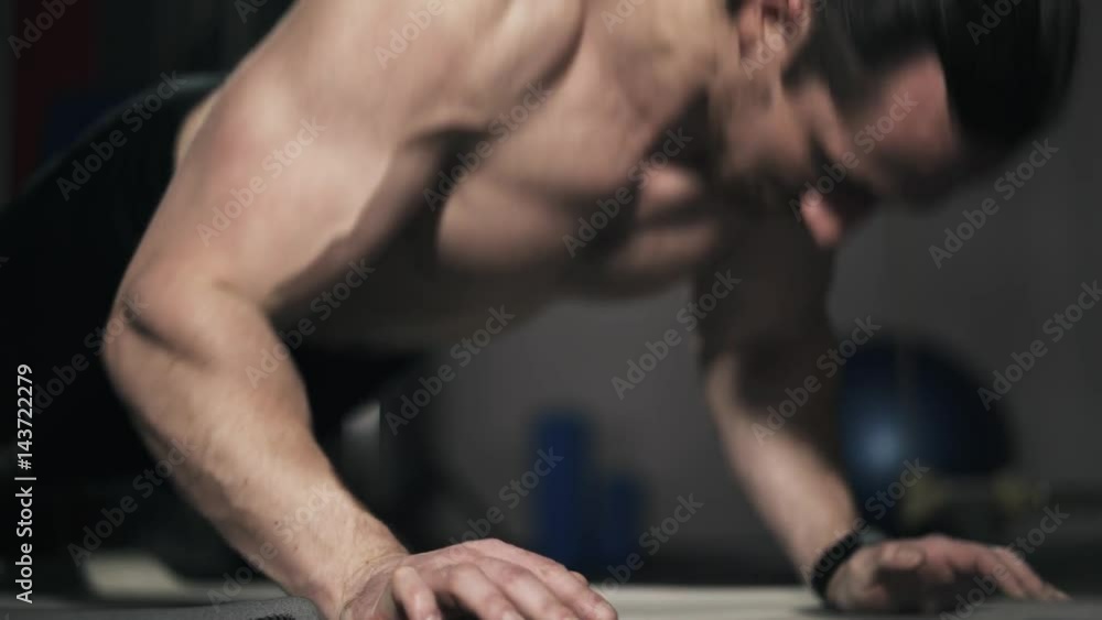 Close up of a young bearded man with long hair and bare torso doing push ups in a gym. Locked down real time close up shot.
