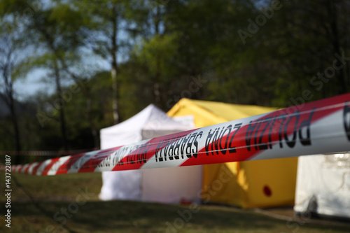 Red and white police line around a crime scene tent in a forest