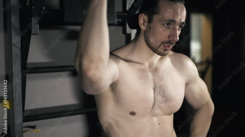 Front view of a bearded young bodybuilder with a naked torso breathing heavily after an intensive workout in a gym. Real time tilt up medium shot Front view of a bearded young bodybuilder with a naked torso breathing heavily after an intensive workout in a gym. Real time tilt up medium shot