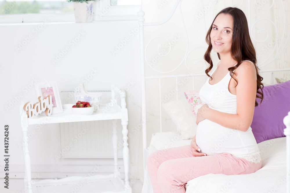 Happy pregnant woman sitting on the bed. A young pregnant woman is sitting in the bedroom. Pregnant woman relaxing. Happy pregnant woman sitting on the bed. A young pregnant woman is sitting in the bedroom. Pregnant woman relaxing.