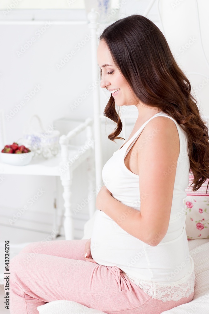 Happy pregnant woman sitting on the bed. A young pregnant woman is sitting in the bedroom. Pregnant woman relaxing.