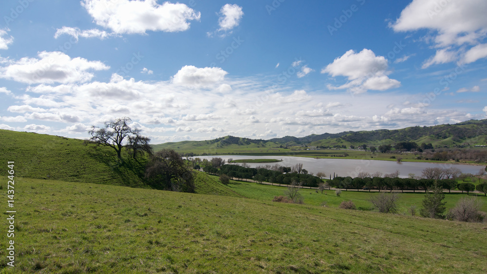 Panoramic view of the Lagoon Valley Park in Vacaville, California, USA, featuring the chaparral in the winter with green grass, and the lake, with interesting clouds in the sky