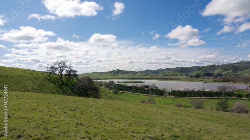 Panoramic view of the Lagoon Valley Park in Vacaville  California  USA  featuring the chaparral in the winter with green grass  and the lake  with interesting clouds in the sky