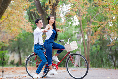 photo of cute couple sitting on bicycle and holding hands on the wonderful autumn park background