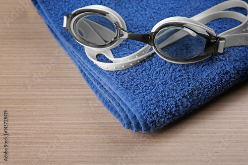 Swimming goggles with towel on wooden background