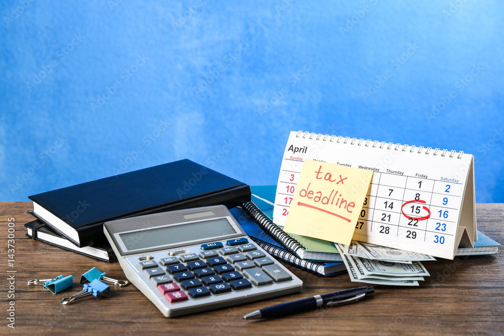 Paper sheet with text TAX DEADLINE, calculator and notebooks on wooden table Paper sheet with text TAX DEADLINE, calculator and notebooks on wooden table