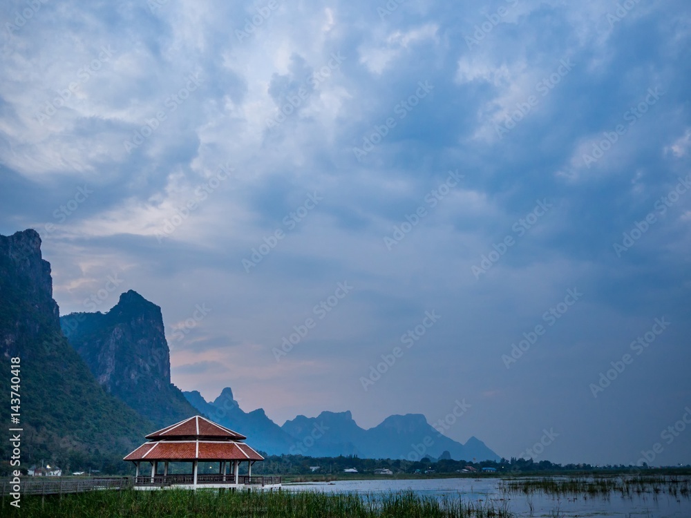 Red roof pavilion over lotus marsh with moutains silhouette and cloudy morning sky as background in Sam Roi Yot National Park, Thailand