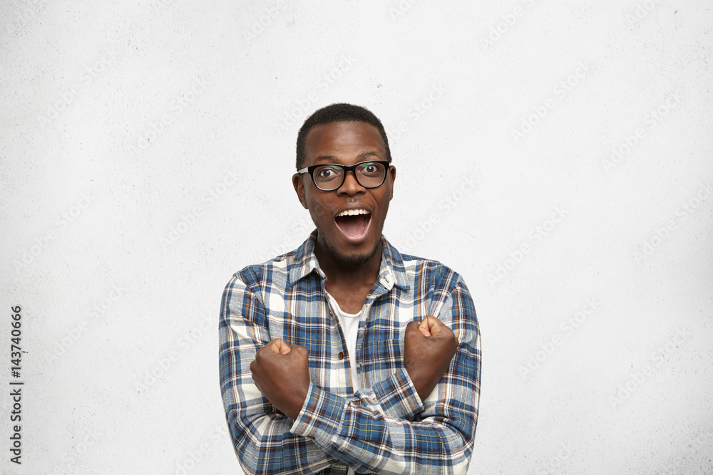 Portrait of handsome young dark-skinned male dressed in stylish clothes exclaiming in excitement, feeling happy after having asked a girl out on date and she said 'Yes'. Human emotions and feelings Portrait of handsome young dark-skinned male dressed in stylish clothes exclaiming in excitement, feeling happy after having asked a girl out on date and she said 'Yes'. Human emotions and feelings