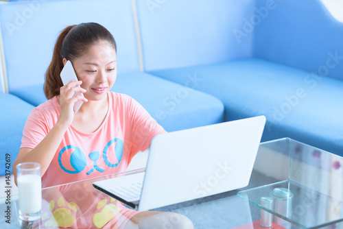 Asian Chinese young woman using laptop and smart phone in home.