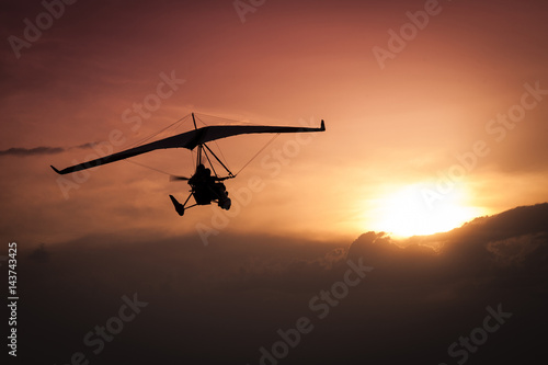 Weight-Shift ultralight aircraft silhouette in the sunset, above stormy clouds