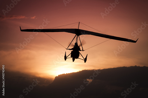 Weight-Shift ultralight aircraft silhouette  in the sunset, above stormy clouds photo