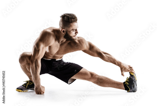 Man stretching his hamstrings. Photo of sporty man doing exercising on white background. Sports