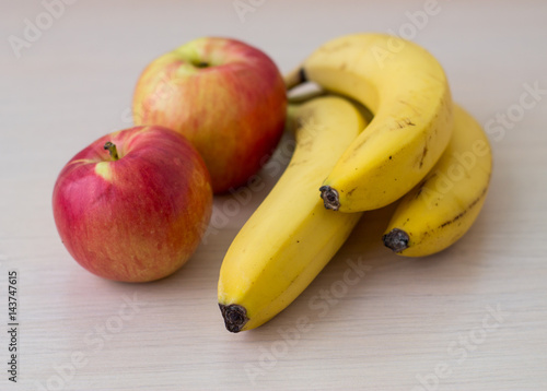 Two apples and bananas on a light wood background.