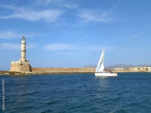 White Yacht Sailing along the Medieval Lighthouse on the Blue Aegean Sea, Crete Island, Greece 