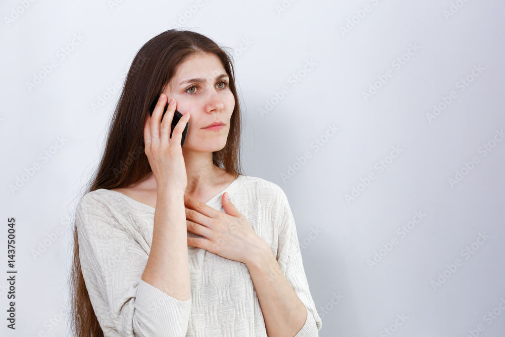 Portrait of a distressed young woman talking on the phone and having received bad news. Human reaction, expression. Grey background. Portrait of a distressed young woman talking on the phone and having received bad news. Human reaction, expression. Grey background.