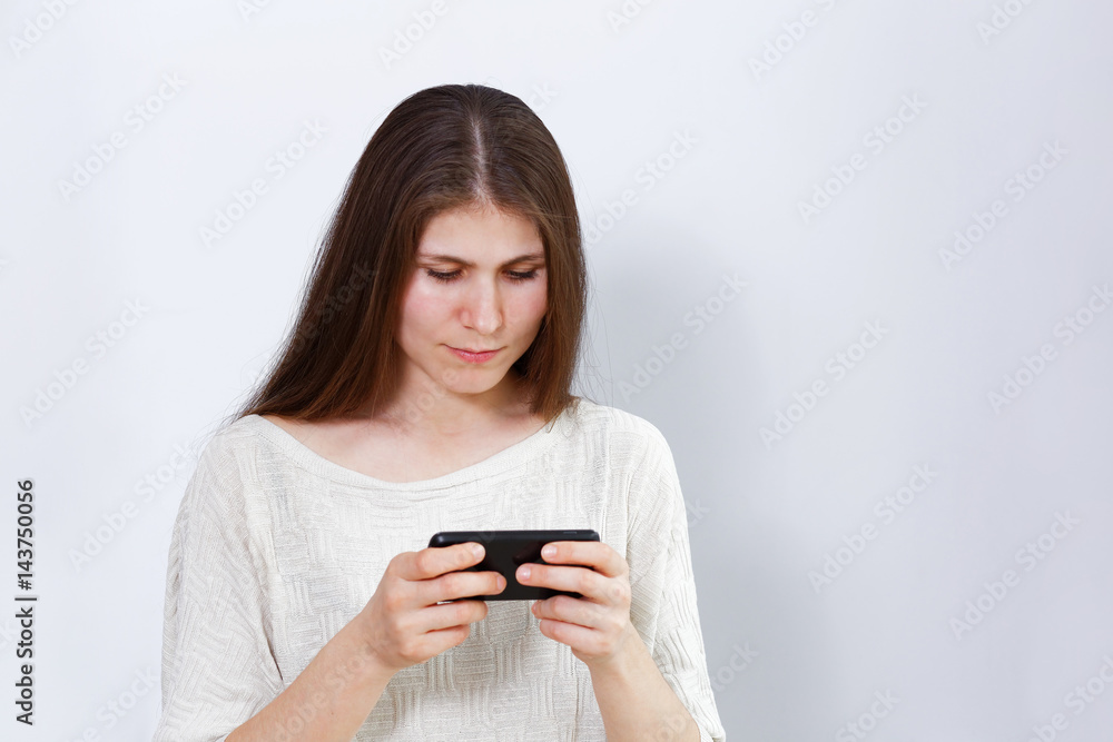 Portrait of a young woman playing a game or watching a movie on the smartphone. Grey background. Portrait of a young woman playing a game or watching a movie on the smartphone. Grey background.