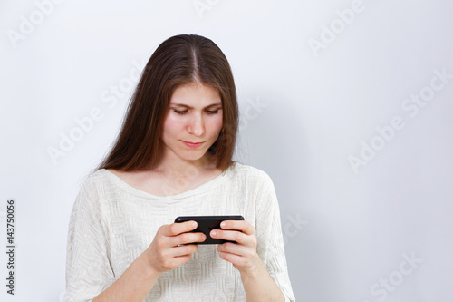 Portrait of a young woman playing a game or watching a movie on the smartphone. Grey background.