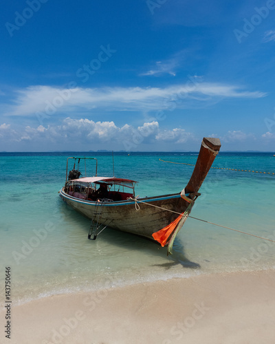 Wooden boat on a turquise blue sea with white clouds on a horizon © Sead