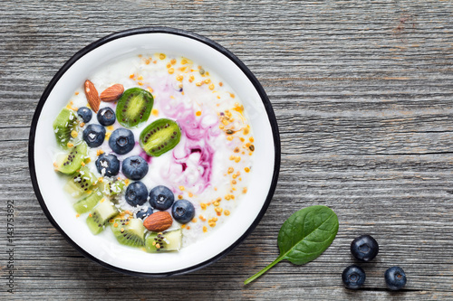 Smoothie bowl with blueberries, kiwi, almonds, coconut, chia seeds and bee pollen. Top view, rustic wooden background, copy space