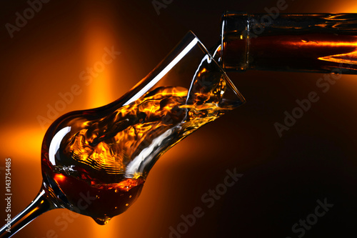 Pouring alcoholic drink into a glass on dark background