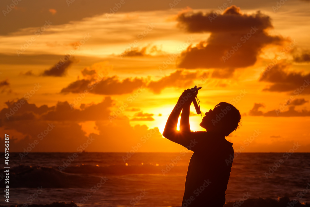 Silhouette of man taking photo on the beach during sunset.