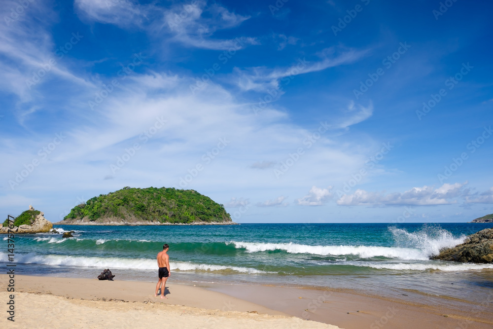 A man stands on the beach and watching the waves.