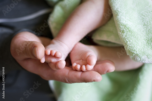 Baby in father's hands. Both parents support child's feet with his hands. Close up. photo