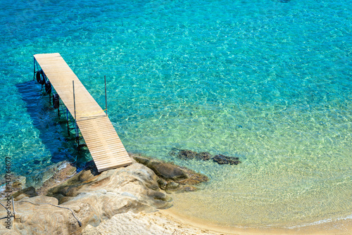 Obraz na płótnie Wooden walking bridge over clear sea water, taken on a sunny day. Photo from Megali Amos Beach, Ammouliani Island, Chalkidiki, Greece. w salonie