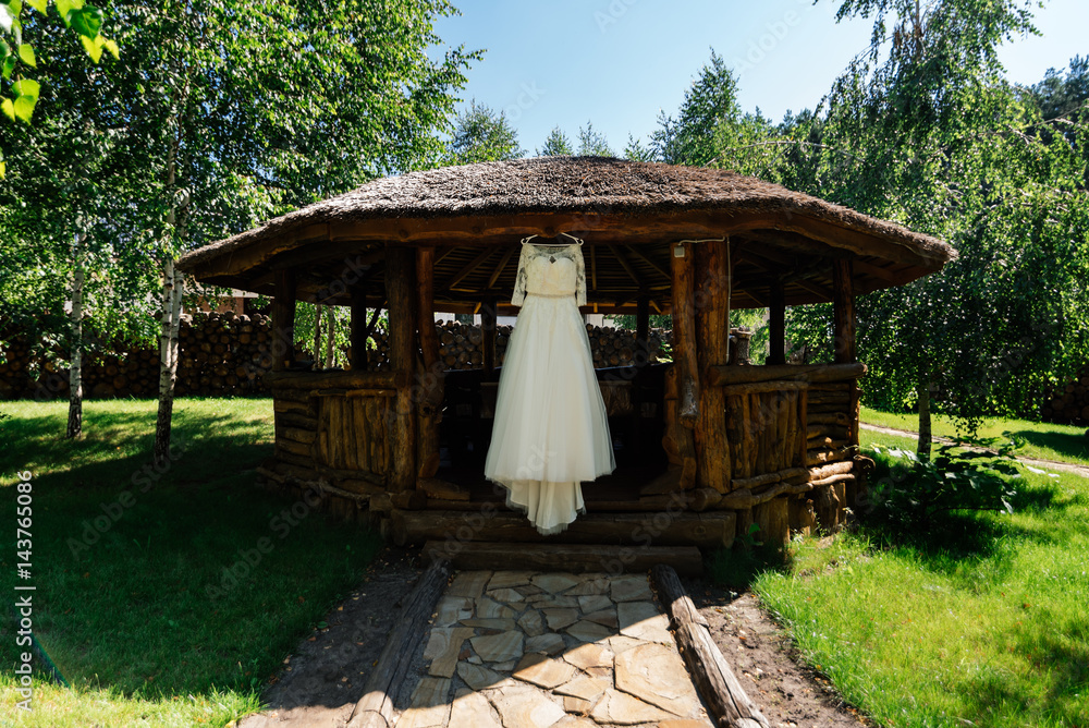 Beautiful wedding dress hanging on the wooden arbor next to the birch outdoors Beautiful wedding dress hanging on the wooden arbor next to the birch outdoors