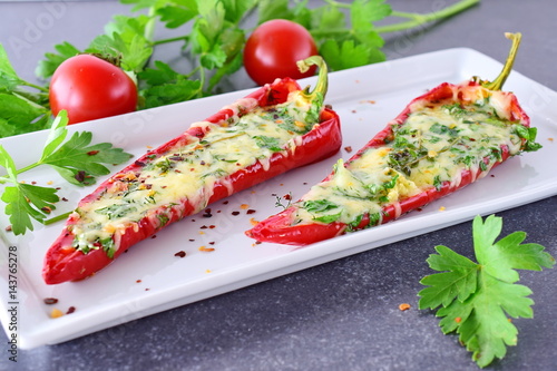 Oven cooked red paprika stuffed with cheese, garlic and herbs on a white plate with parcley and cherry tomatoes an abstract grey background. healthy eating concept. Mediterranean lifestyle. photo