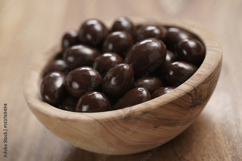 chocolate covered almonds in wood bowl on table, closeup chocolate covered almonds in wood bowl on table, closeup