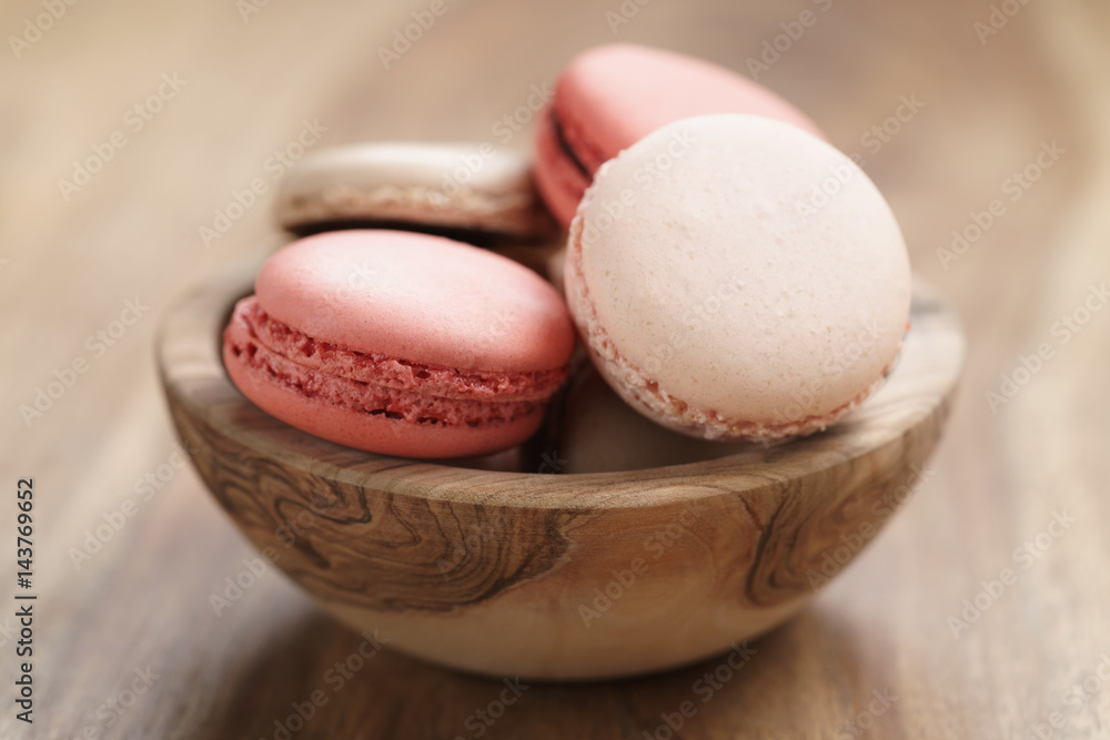 pastel colored macarons with strawberry, rose and caramel flavour in wood bowl on table pastel colored macarons with strawberry, rose and caramel flavour in wood bowl on table
