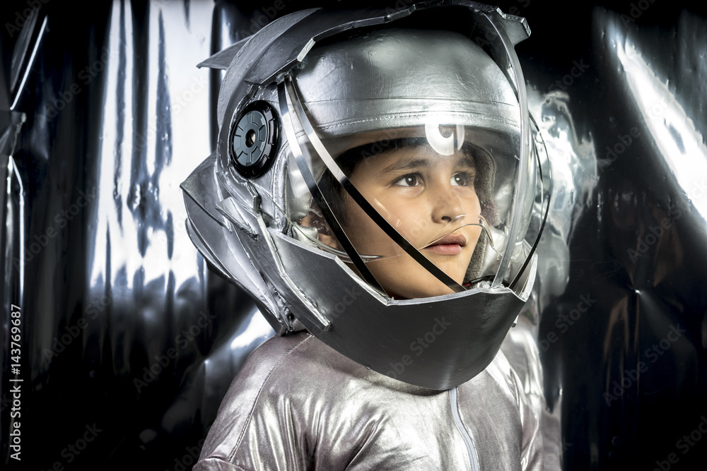 Boy playing to be an astronaut with a space helmet and silver suit on metallic background
