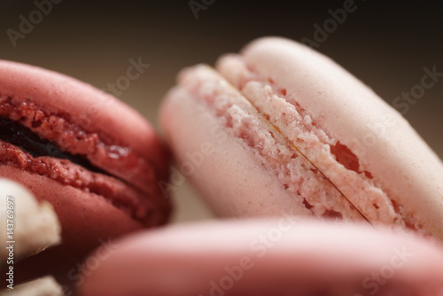 closeup shot of pastel colored macarons with strawberry, rose and caramel flavour in wood bowl, macro photo