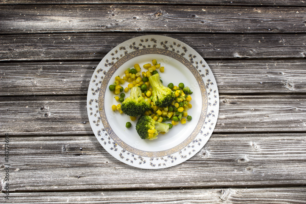 Gray old plank table and broccoli, corn, green peas on a plate for lunch Gray old plank table and broccoli, corn, green peas on a plate for lunch