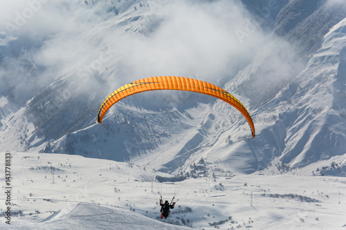 Parachute sky-diver flying in clouds above mountains with fresh snow on Sunny winter day in the ski resort. Travel adventure concept. space for text