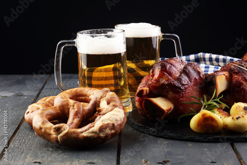 Baked pork shank and honey sause and glass of beer on a dark wooden table.