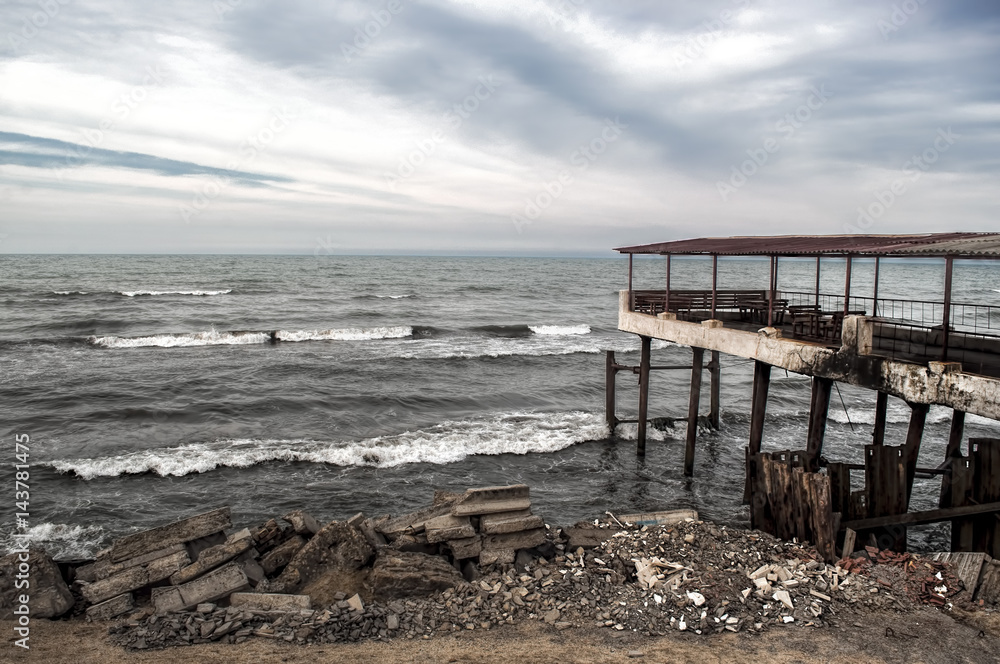 Beautiful surreal landscape of abandoned house and ladder on rocky seashore at sunset time. Cloudy weather. Caspian Sea, Azerbaijan,