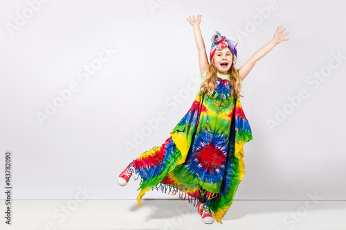 Happy blonde child girl in hippie colorful dress against white wall