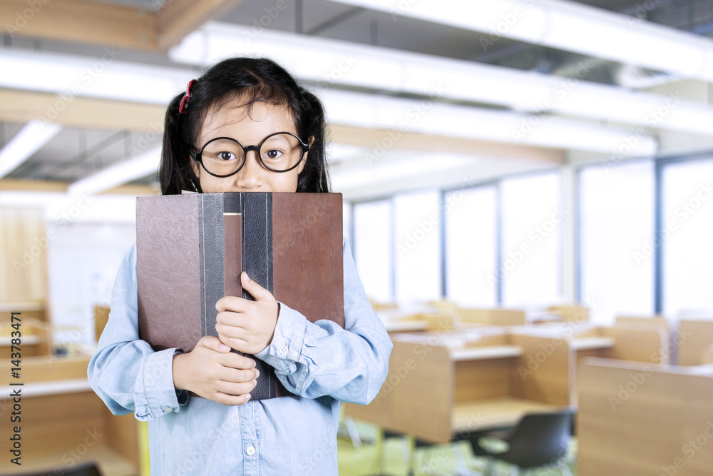 Little girl hiding behind book in classroom Little girl hiding behind book in classroom