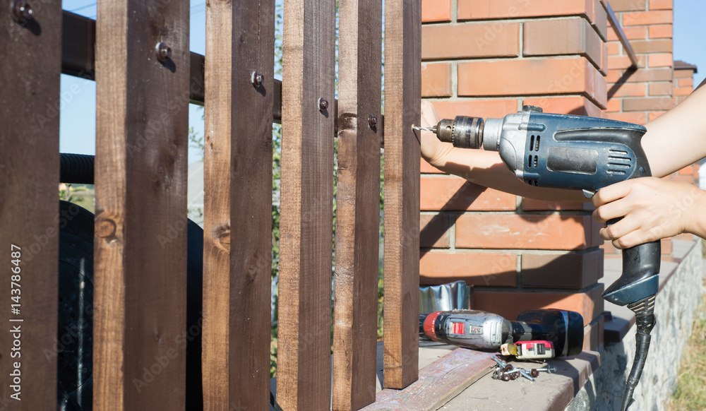 Woman hands drilling wood plank fence to metal construction. Building a wooden fence with a drill and screw. Woman hands drilling wood plank fence to metal construction. Building a wooden fence with a drill and screw.