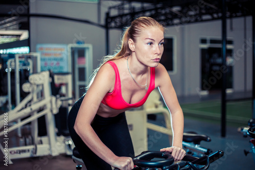 Young sporty woman wearing in sportswear, doing exercise on bicycle in the gym