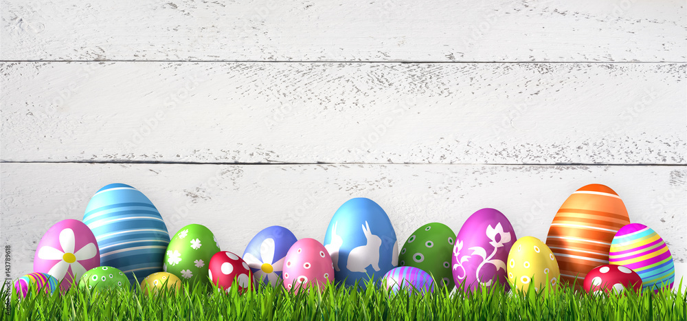 Fototapeta premium Bunte Ostereier im Gras vor weißer Holzwand