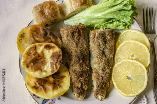 Fried fish with bread, baked potatoes and slices of lemon with lettuce leaf
 photo