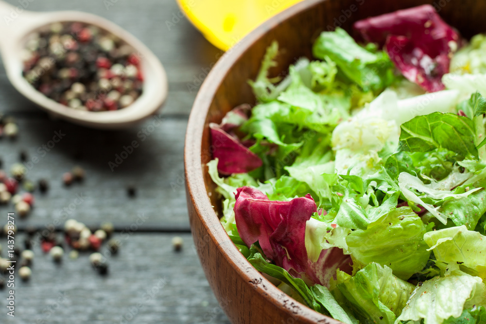 A dish of fresh salad frisse, Romano and radiccio with olive oil, salt and freshly ground percec in a wooden bowl A dish of fresh salad frisse, Romano and radiccio with olive oil, salt and freshly ground percec in a wooden bowl