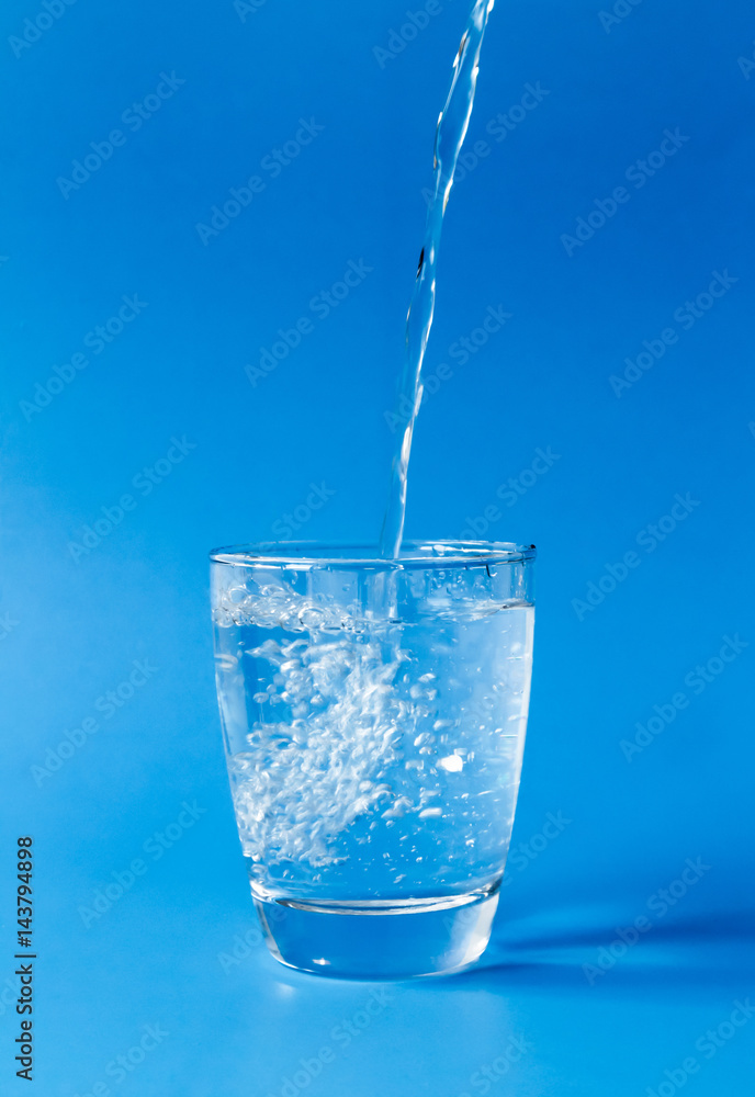 Pouring water into glass on blue background Pouring water into glass on blue background